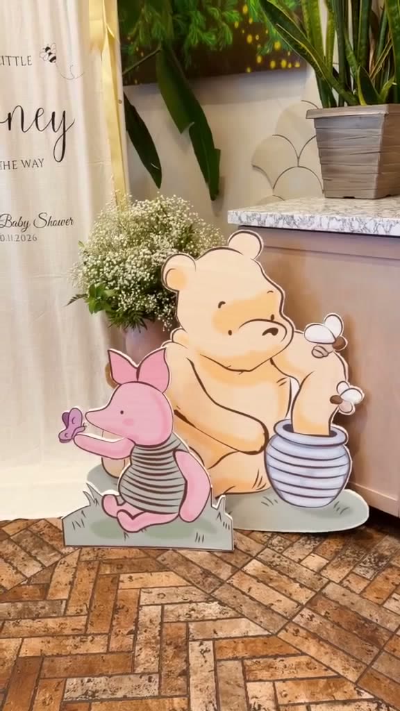 Storybook character foam cutouts beside a printed linen backdrop at a baby shower